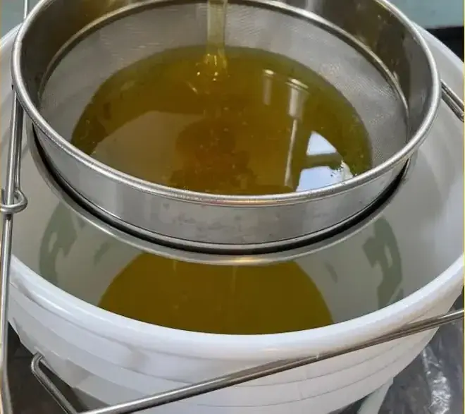 Miel qui coule dans un tamis fin au-dessus d’une chaudière